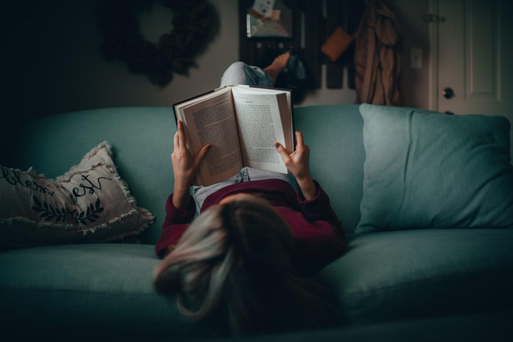 girl lying upside down on couch reading